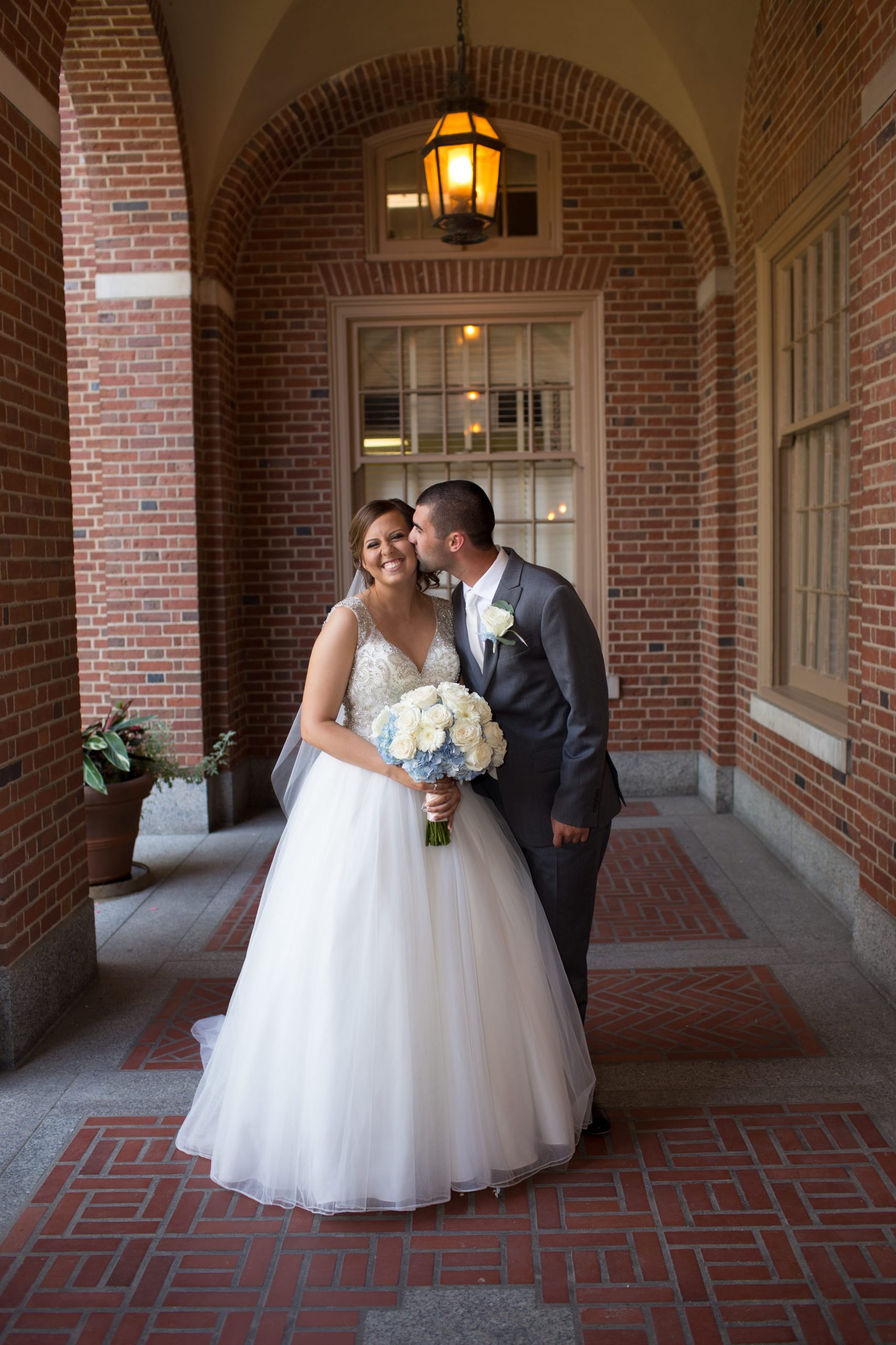 groom kissing bride on cheek under brick archway