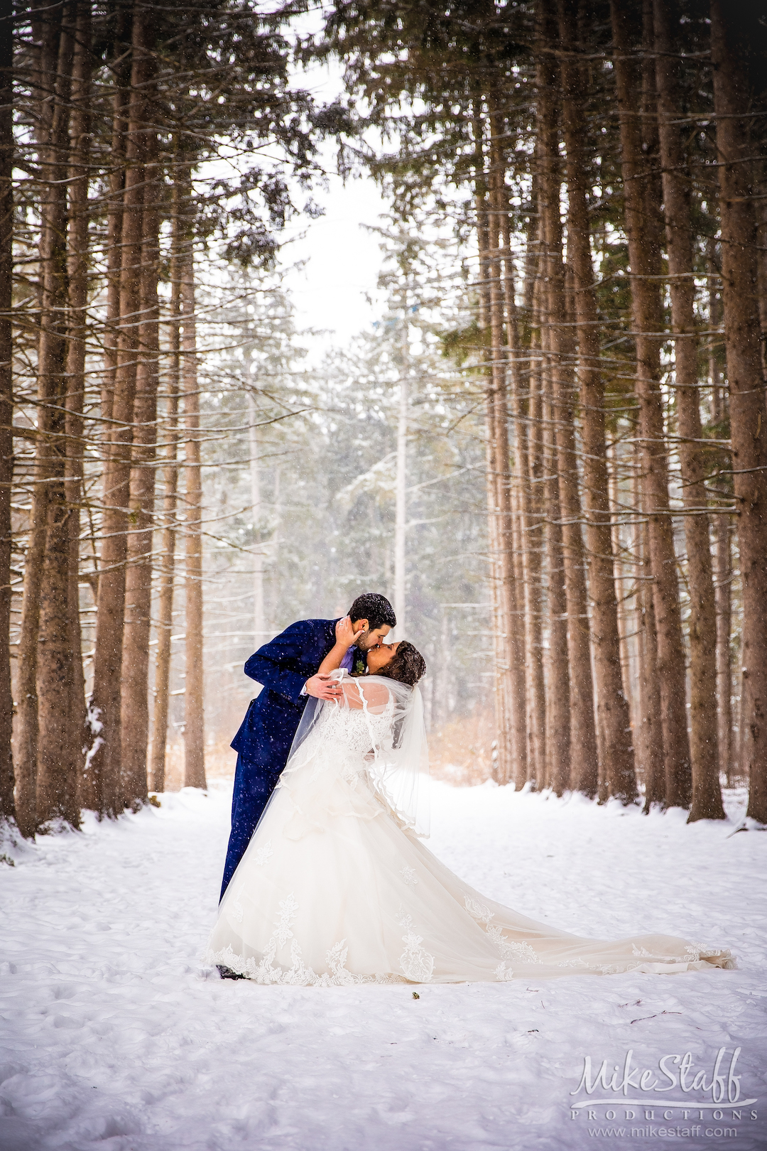 groom kissing bride outside in snow and woods